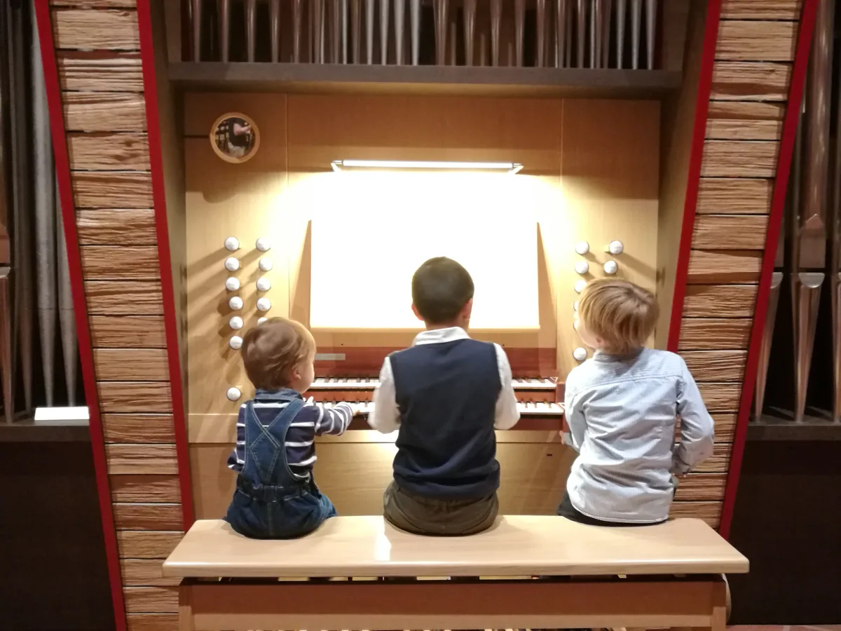 Drei kleine Kinder sitzen vor einer Orgel.